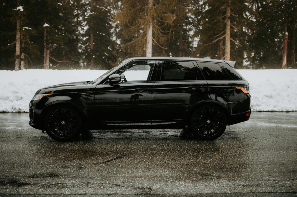 Stylish black SUV parked on a snowy forest road during winter, showcasing automotive elegance.